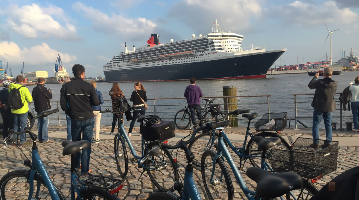 Fahrradtour am Fischmarkt Hamburg schaut auf das Kreuzfahrtschiff Queen Mary 2